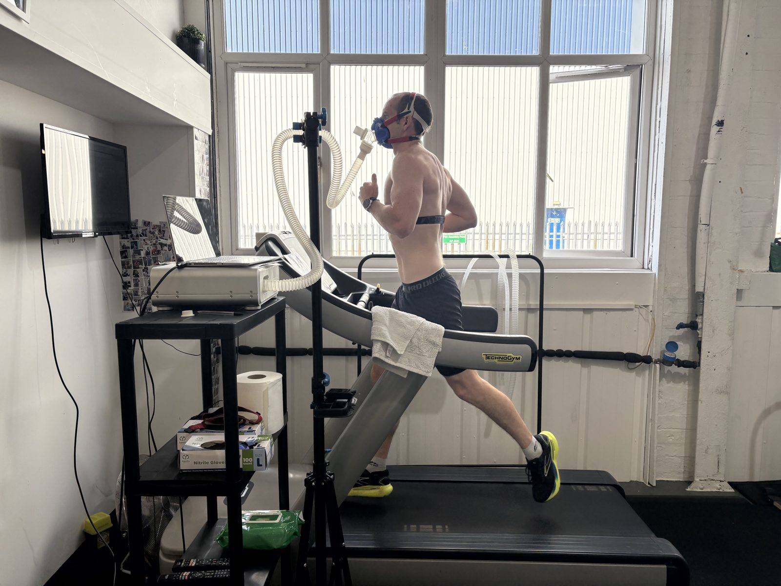 Runner mid-stride on the treadmill during a VO2max step test, wearing a mask and heart-rate monitor